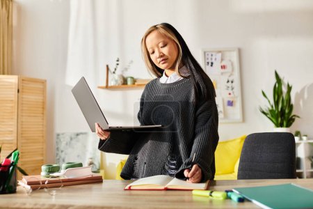 A young Asian girl engaged in e-learning at home, standing in front of a laptop computer.