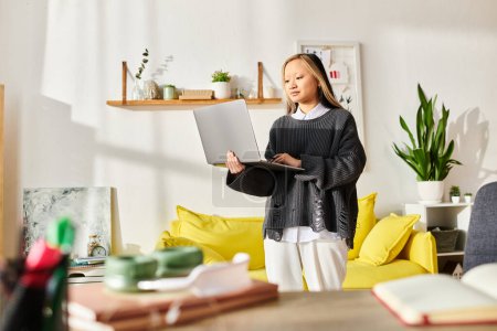 Eine junge Asiatin steht elegant in einem modernen Wohnzimmer und ist in E-Learning vertieft, während sie einen Laptop in der Hand hält..