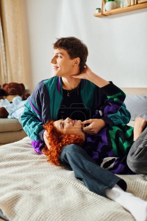 Téléchargez les photos : Séduisante femme gaie aux cheveux roux couchée au lit avec son beau petit ami joyeux tout à la maison - en image libre de droit