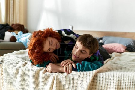ansprechende lustige Mann entspannt sich im Bett neben seiner rothaarigen schönen Freundin, während zu Hause