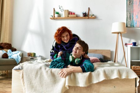 Téléchargez les photos : Homme attrayant avec écouteurs couché dans le lit avec sa copine aux cheveux rouges attrayante à la maison - en image libre de droit