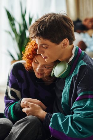 attractive young man with headphones hugging his beautiful stylish girlfriend near bed at home