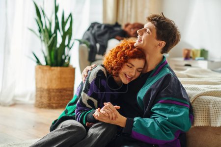 Téléchargez les photos : Séduisant couple joyeux dans des vêtements à la mode vibrante étreignant amoureusement à la maison - en image libre de droit