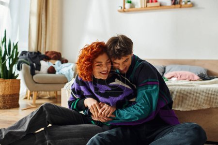 good looking loving joyous couple in vibrant clothes having great time and hugging while at home