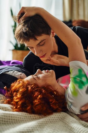 junges attraktives Paar in lebendiger Hauskleidung bereitet sich darauf vor, sich verführerisch zu küssen, während sie zusammen im Bett liegen