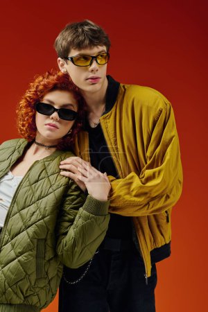 Téléchargez les photos : Beau couple aimant dans des vêtements à la mode avec des lunettes de soleil posant ensemble sur fond rouge - en image libre de droit