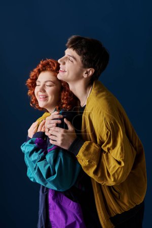 Téléchargez les photos : Joyeux couple attrayant dans des vêtements élégants colorés étreignant amoureusement et souriant joyeusement - en image libre de droit