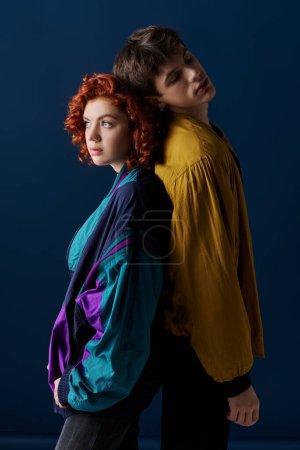 Foto de Atractivo novio y novia posando espalda con espalda y mirando hacia otro lado sobre fondo azul oscuro - Imagen libre de derechos