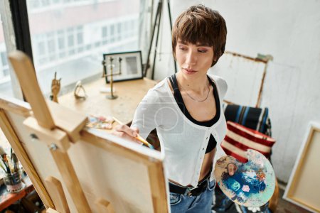Eine Frau steht an einer Staffelei und hält konzentriert und kreativ einen Pinsel in der Hand.