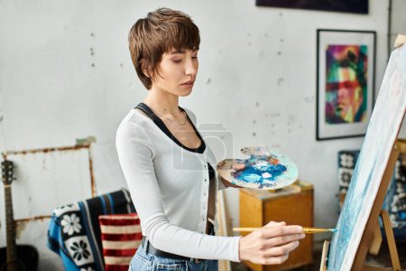 A woman holding a paintbrush in front of a painting.
