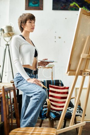 A woman seated in front of an easel, focusing on her artwork.