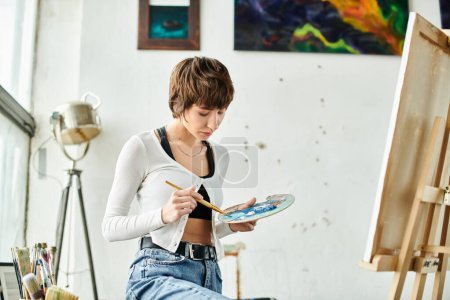 A woman sits on a chair with a paintbrush and palette.