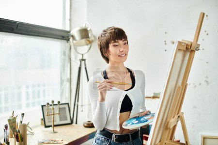 A woman holds a paintbrush and palette.