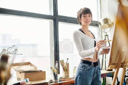 Woman with paintbrush standing in front of easel.