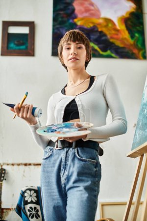 A woman holds a paintbrush and a palette.