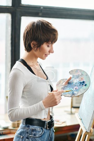 A woman holds a paintbrush and palette with focus and precision.