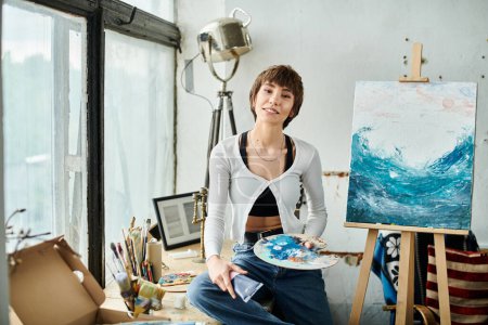 Téléchargez les photos : Une femme s'assoit devant une peinture, tenant délicatement une palette. - en image libre de droit