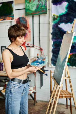 Mujer en pinturas top negras con pincel y paleta.