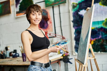 A woman holds a paintbrush in front of a painting.