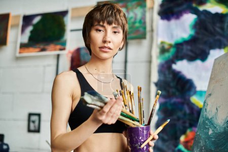 A woman gracefully holding a purple cup filled with paint brushes.