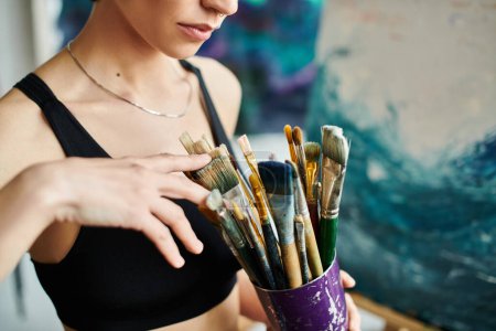 Eine Frau hält einen Becher voller Pinsel in der Hand, bereit, etwas Schönes zu erschaffen.