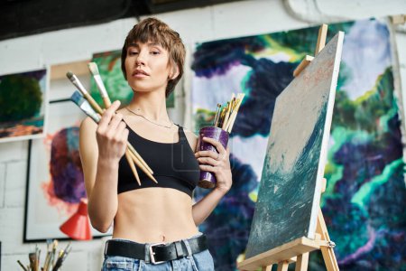 A woman in a black top holds a paintbrush.