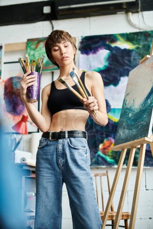 A woman in a black tank top holds paintbrushes.