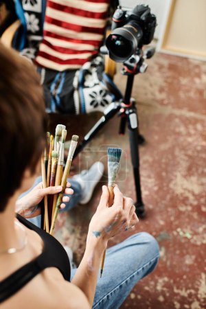 Téléchargez les photos : Une femme assise sur le sol, immergée dans la peinture avec un pinceau vibrant. - en image libre de droit
