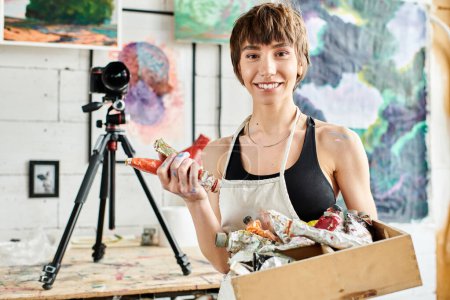 A woman holding a box of paint in front of a camera.