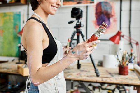 Woman holding a bottle of paint in a vibrant studio.