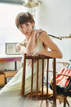 A woman elegantly sits on top of a wooden chair.