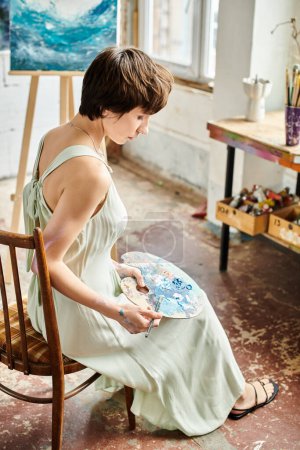 A woman sits peacefully in a chair, delicately holding a palette in her hands.