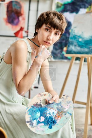 Foto de Una mujer se sienta a pintar frente a una obra de arte cautivadora, sosteniendo un pincel. - Imagen libre de derechos
