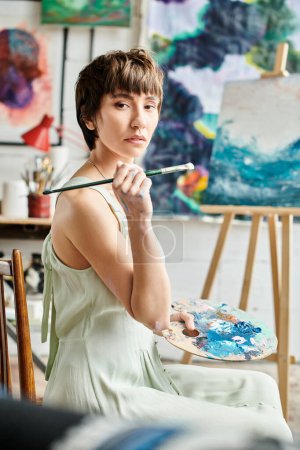 Foto de Una mujer se sienta delante de una pintura, pincel en mano. - Imagen libre de derechos