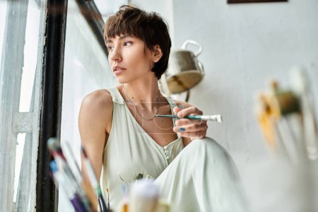 Téléchargez les photos : Une femme s'assoit sur un rebord de fenêtre, tenant une brosse. - en image libre de droit