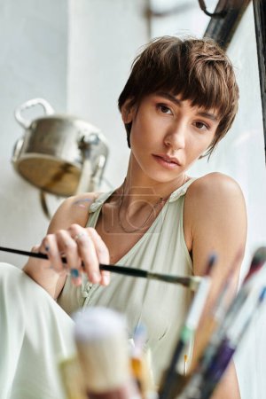 Attractive woman sits on a window sill, holding a brush.