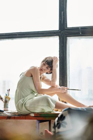 Eine Frau sitzt mit Pinsel auf Fensterbank.