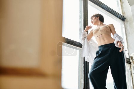 Foto de Una mujer está de pie con confianza delante de una ventana, mostrando su estilo sofisticado. - Imagen libre de derechos