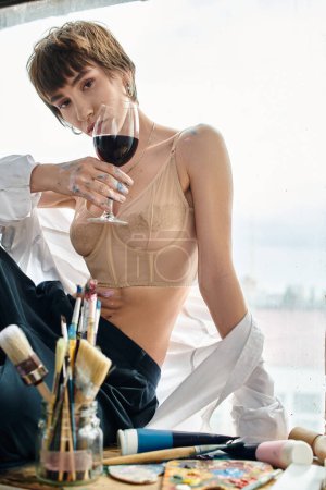 Woman relaxes on window sill, sipping wine.