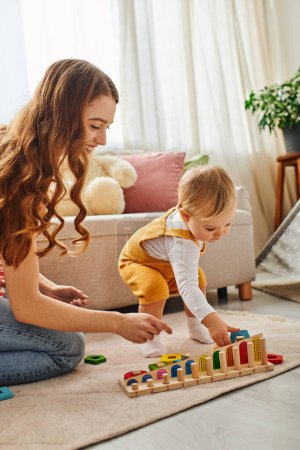 Téléchargez les photos : Une jeune mère joue joyeusement avec sa fille tout-petit sur le sol dans leur maison confortable. - en image libre de droit