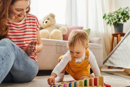 Téléchargez les photos : Une jeune mère interagit joyeusement avec sa fille tout-petit alors qu'ils jouent ensemble sur le sol à la maison. - en image libre de droit