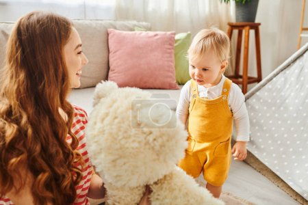 Eine junge Mutter hält liebevoll einen Teddybär in der Hand, während ihre kleine Tochter voller Freude und Zuneigung zusieht.