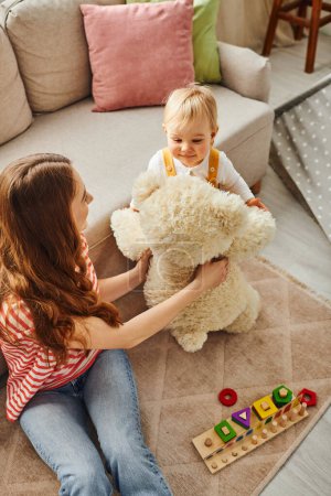 Eine junge Mutter und ihre kleine Tochter spielen fröhlich mit einem Teddybär, teilen Freude und schaffen lebenslange Erinnerungen.