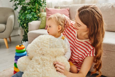 Eine junge Mutter und ihre kleine Tochter, die sich beim Spielen mit einem Teddybär zusammentun, um gemeinsam Erinnerungen zu wecken.