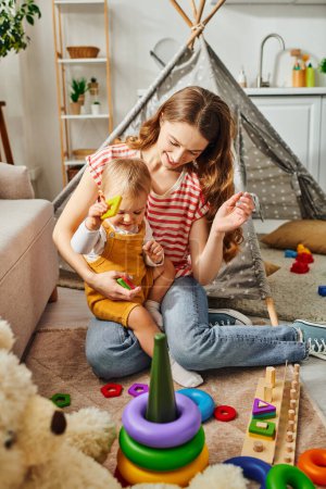 Una joven madre está jugando felizmente con su hija pequeña en una habitación acogedora, construyendo una conexión amorosa y alegre.
