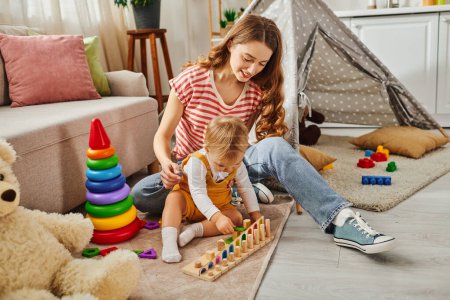 Una joven madre está jugando alegremente con su hija pequeña en el suelo en casa, fomentando un fuerte vínculo a través de actividades divertidas.