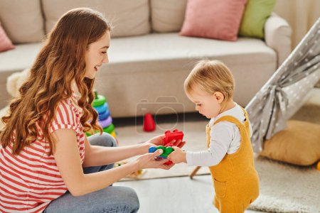 Geschätzte Momente als junge Mutter und ihr Kleinkind teilen Spielzeug und Lachen.