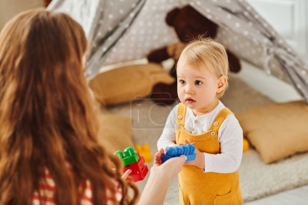 Photo for A young mother happily engages with her toddler daughter, playing together in a cozy room filled with love and joy. - Royalty Free Image
