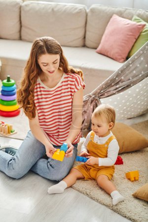 Photo for A young mother sitting on the floor, joyfully engaging with her toddler daughter through play and interaction. - Royalty Free Image