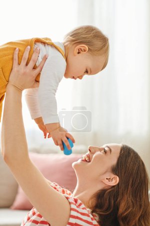 A woman joyfully lifts her toddler daughter high in the air as they bond and enjoy quality time together at home.